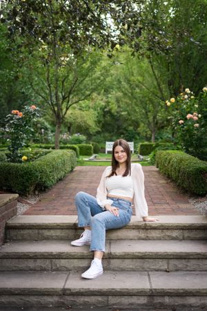 Casual portrait on stone steps surrounded by manicured garden hedges and roses.
