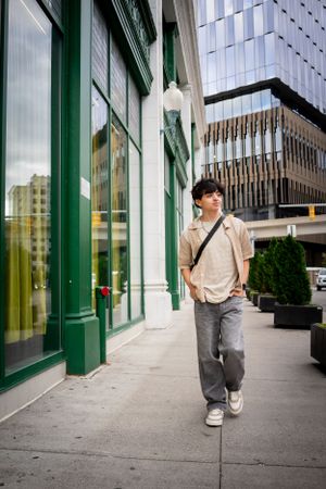 A person in casual attire stands outside a modern building with green trimmed windows and glass facade.