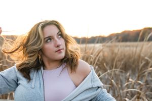 Woman in casual attire sits thoughtfully in golden field during sunset.