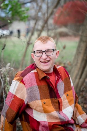 Person in plaid flannel jacket smiling outdoors on cloudy day.