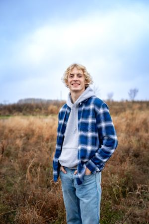 Person in blue plaid flannel and hoodie standing in autumn field against blue sky.