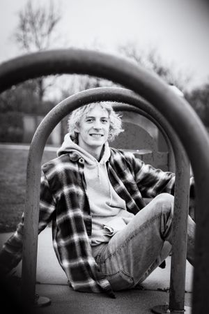 Black and white portrait of person sitting in curved metal playground equipment.