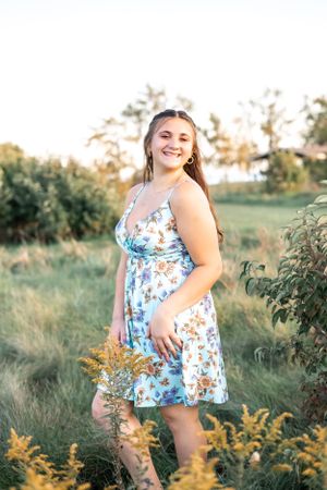 A summer portrait in floral dress among golden wildflowers at sunset.