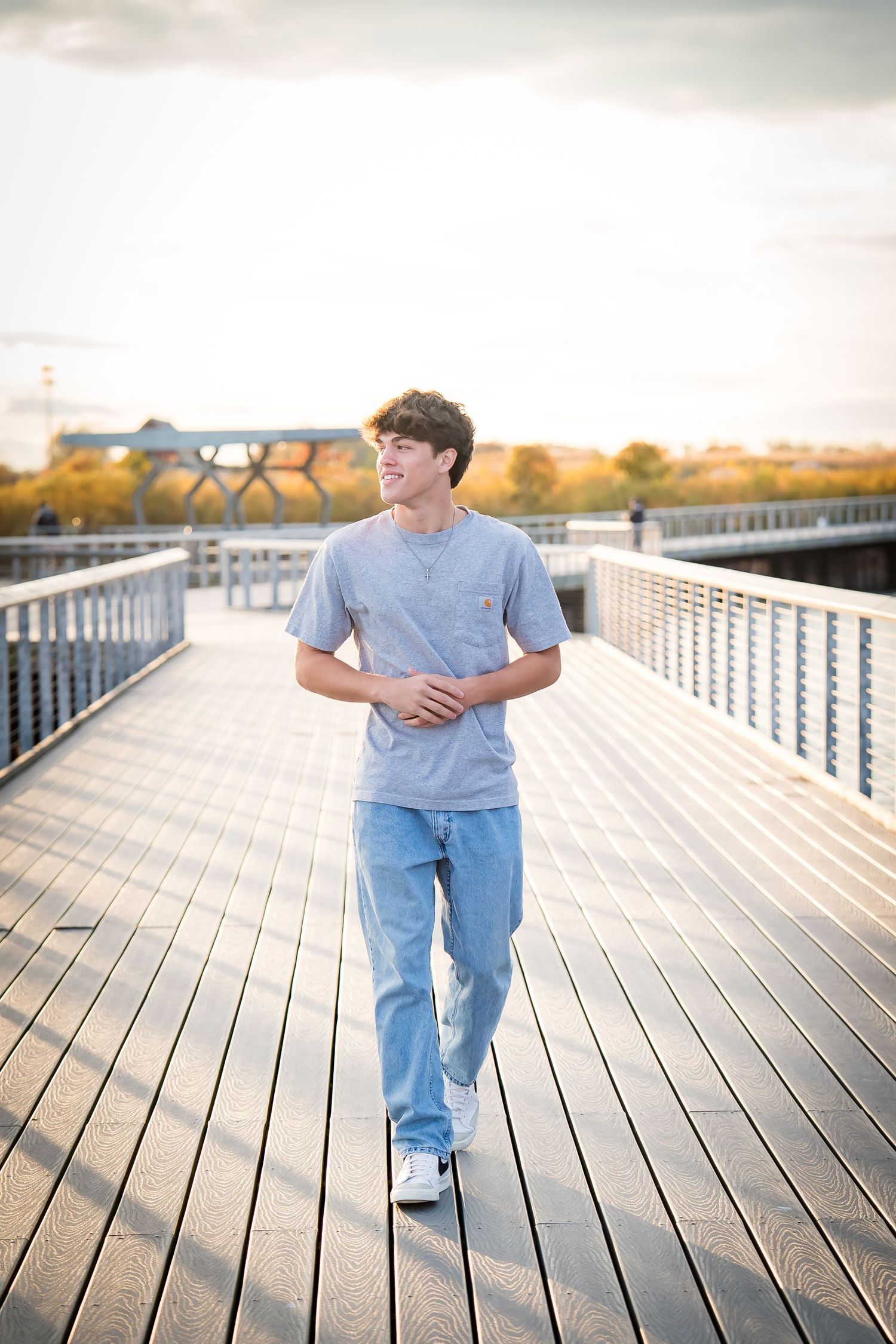 A person in casual attire walks along a wooden boardwalk on a sunny afternoon.