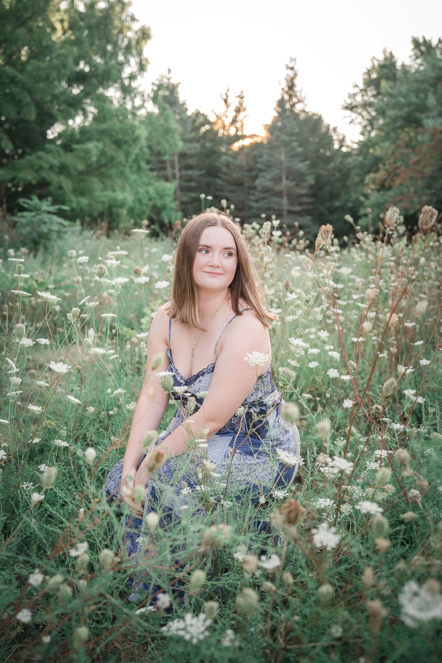 A floral summer dress worn in a dreamy wildflower meadow at sunset with green trees in the background.