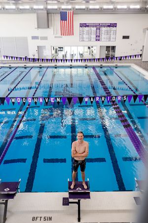 Indoor swimming pool with multiple lanes divided by lane lines and American flag displayed on the wall.