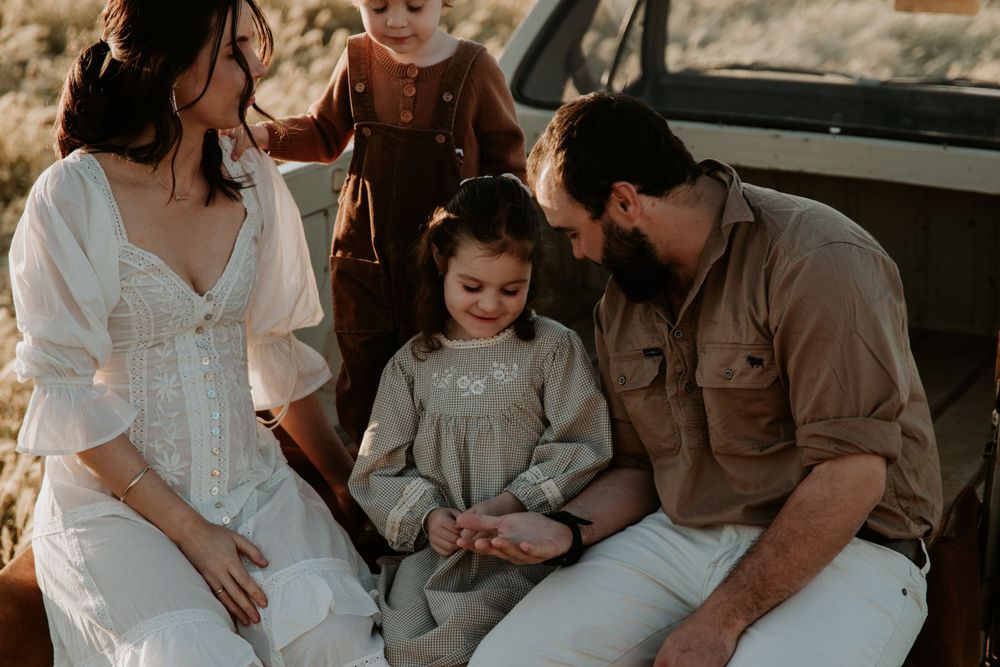 Family enjoying intimate moment together during outdoor photoshoot with classic car.