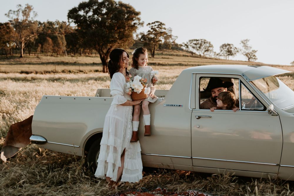 Vintage car parked in a golden field during sunset as people gather around for photos.