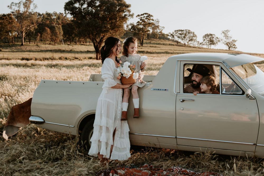 Family gathering around a vintage automobile in a rural field at golden hour.