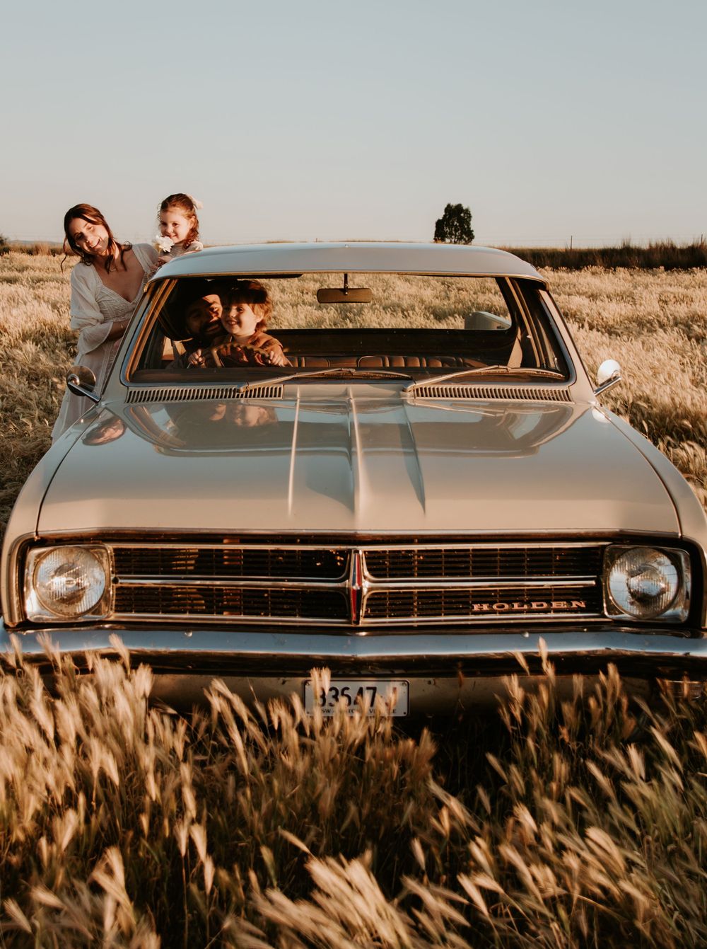 Classic Chevrolet car photographed from different angles in tall grass during sunset.