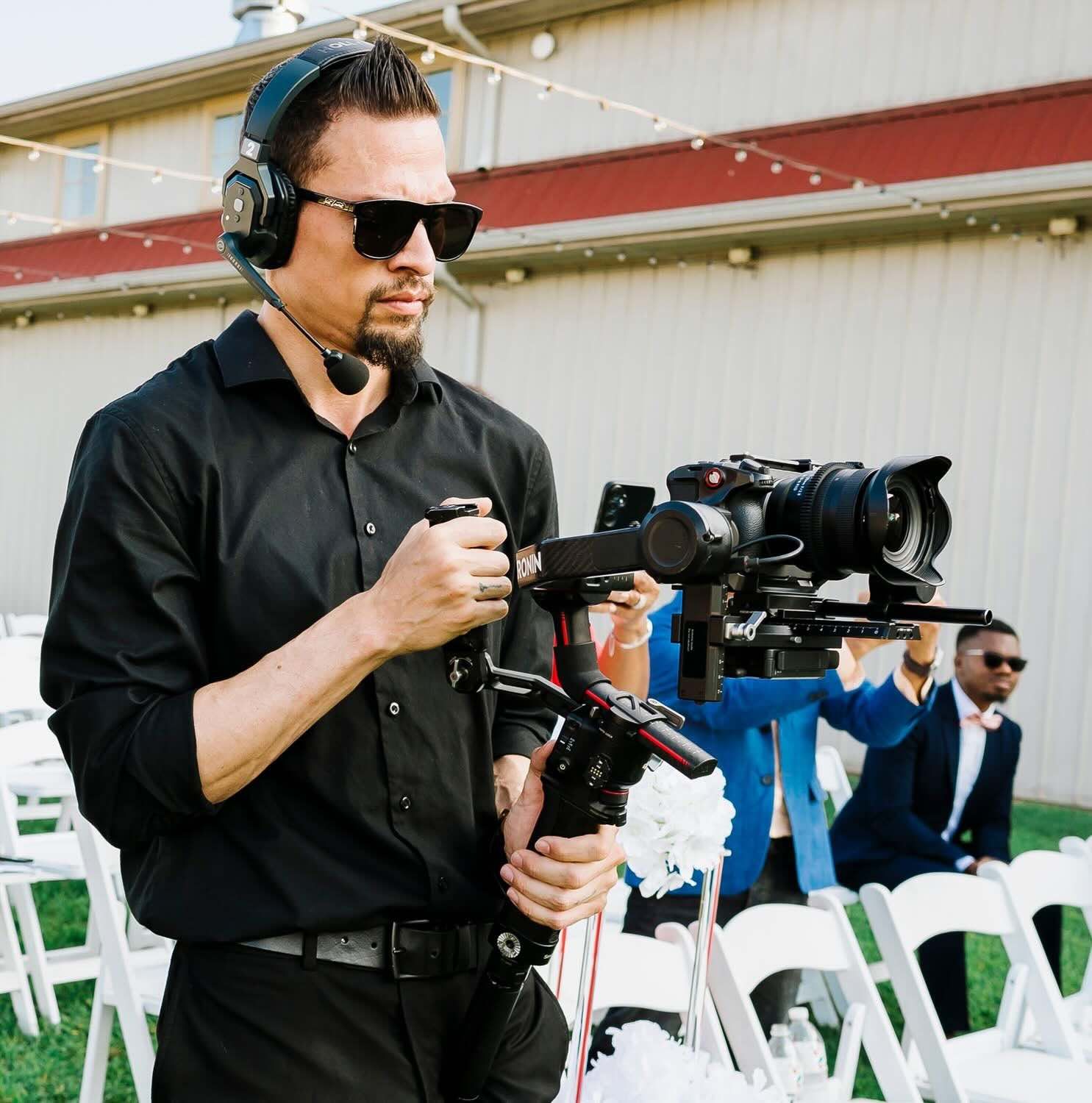 A Baltimore wedding videographer posing for a photo in a black suit on a dark background