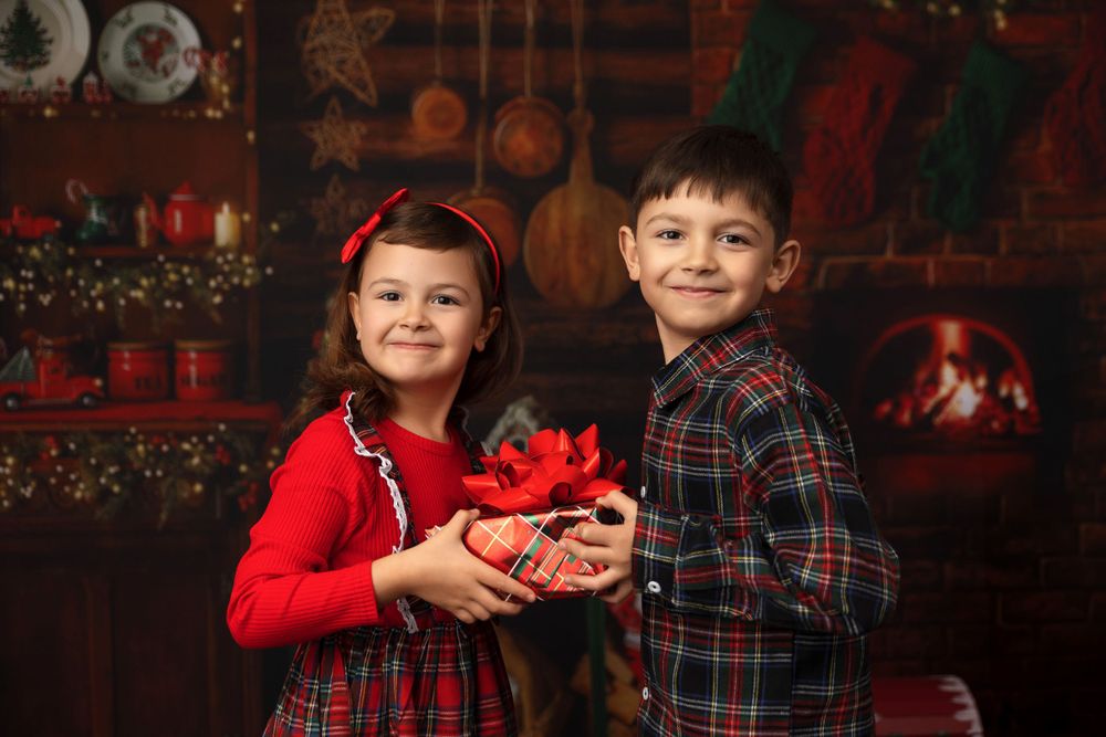 Two children in coordinating red and plaid outfits holding Christmas decorations.