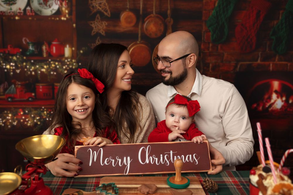 Family poses together with Merry Christmas sign in cozy holiday setting with festive decorations.