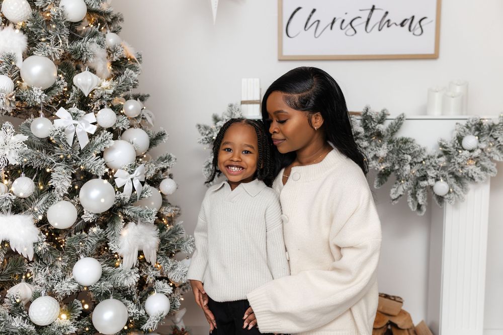 Mother and child in matching cream sweaters smiling beside a white flocked Christmas tree.