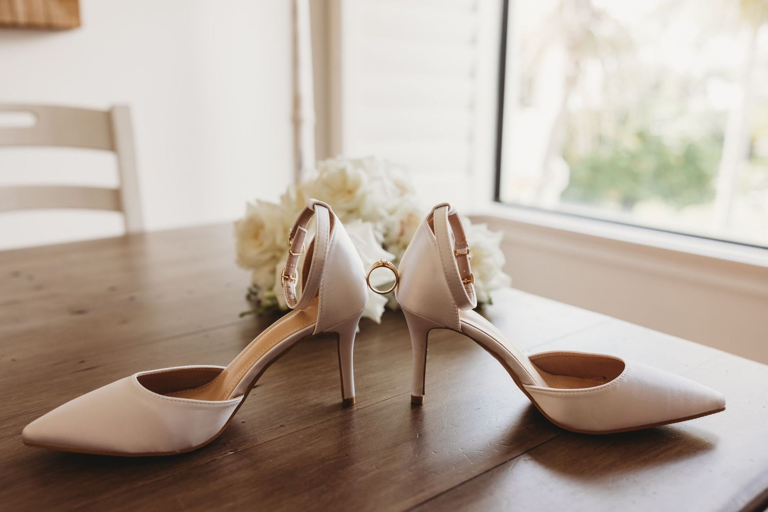 Elegant cream-colored bridal heels with floral details on wooden table.