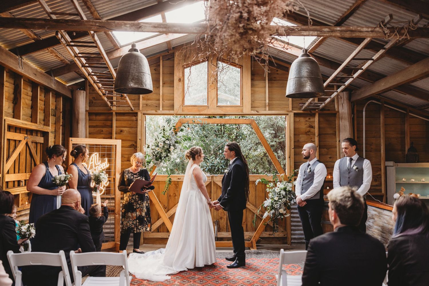 Wedding ceremony in progress inside rustic barn with wooden beams and natural light.