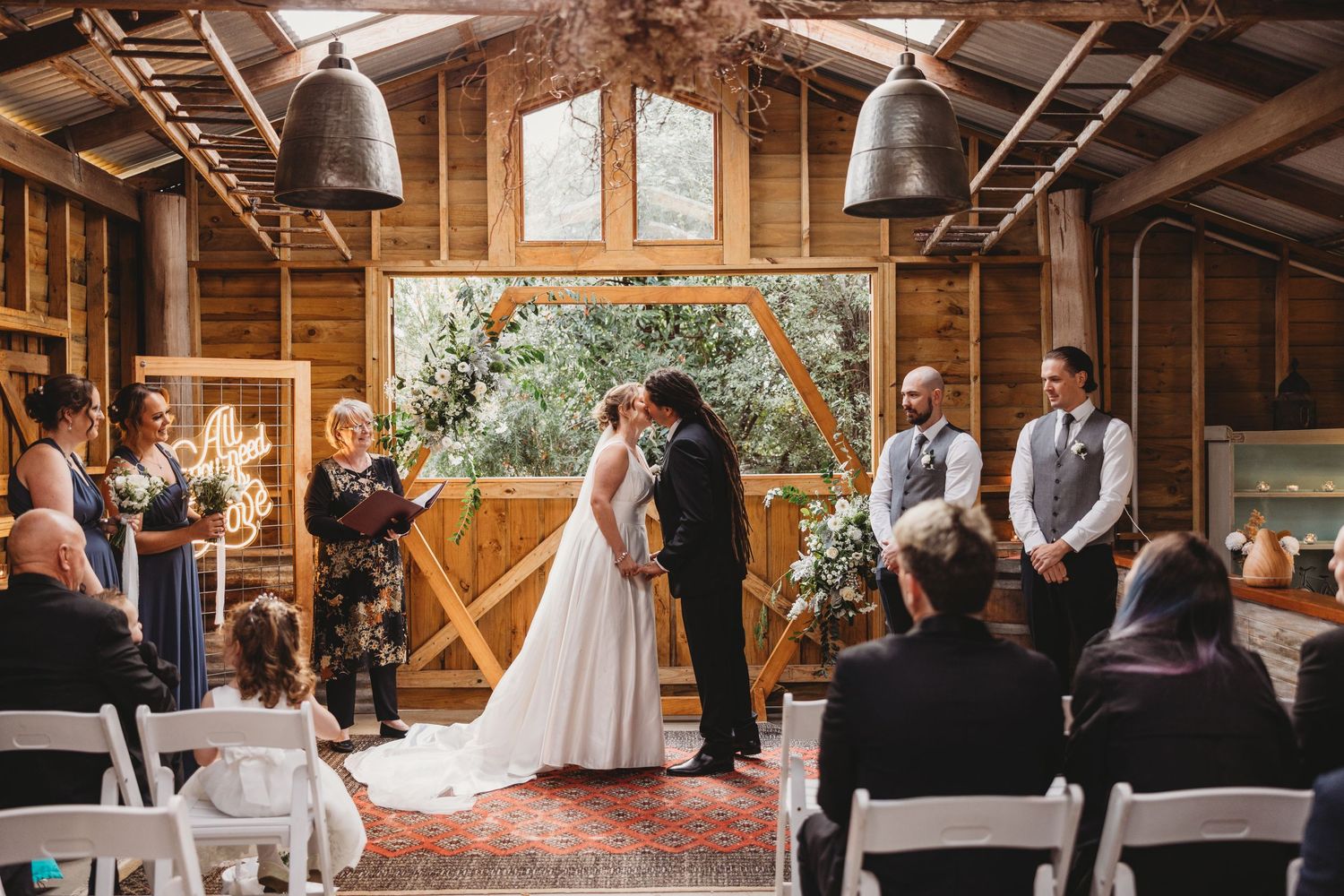 Rustic barn wedding ceremony with wooden beams and natural light streaming through windows.