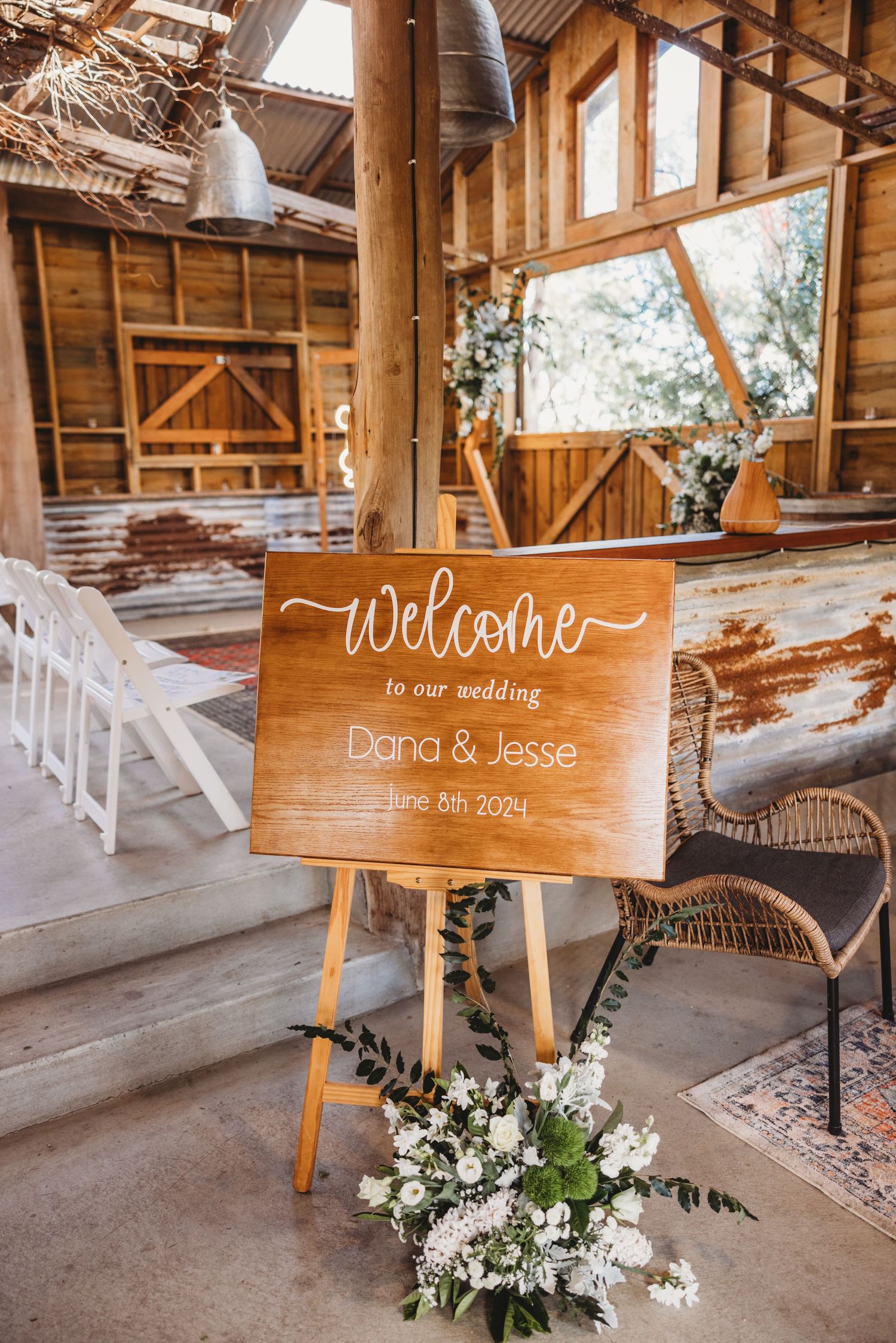 Wooden welcome sign with florals decorates rustic barn wedding venue entrance.