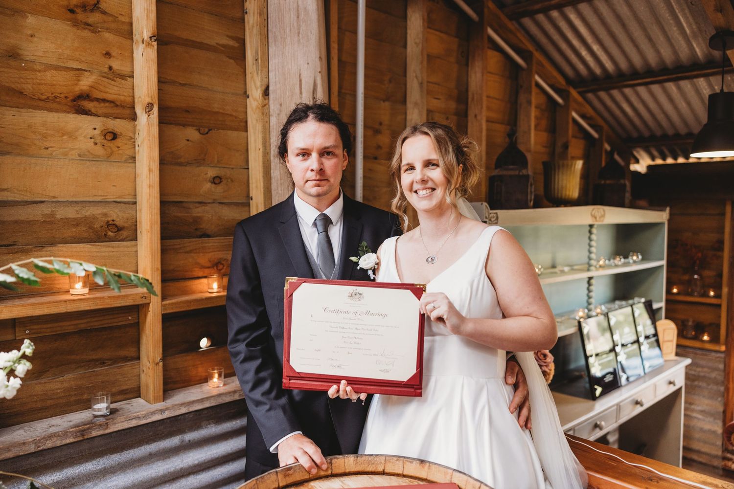Couple holding a red certificate frame inside a rustic wooden venue.