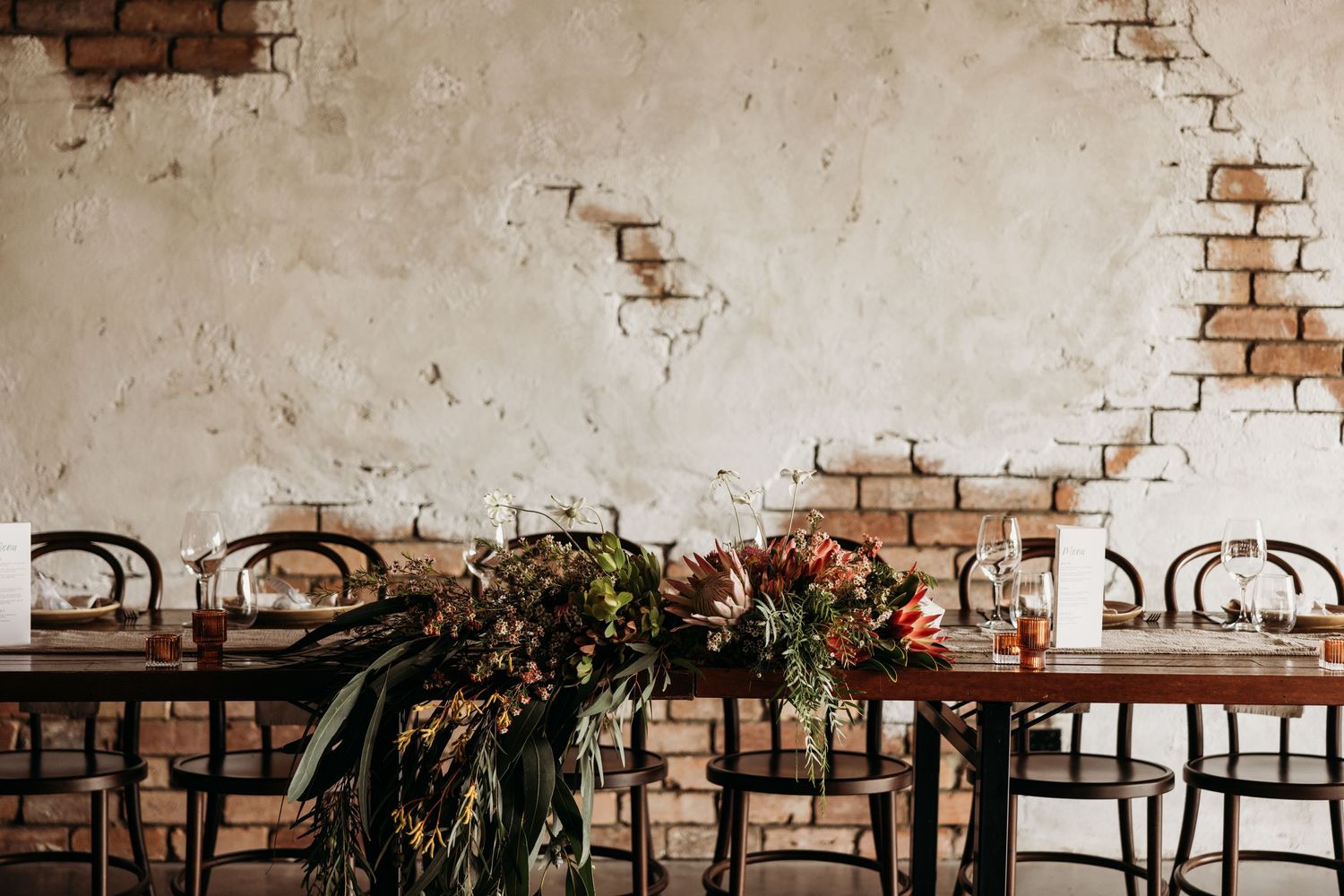 Elegant wedding reception table setup with greenery garland against distressed brick wall.