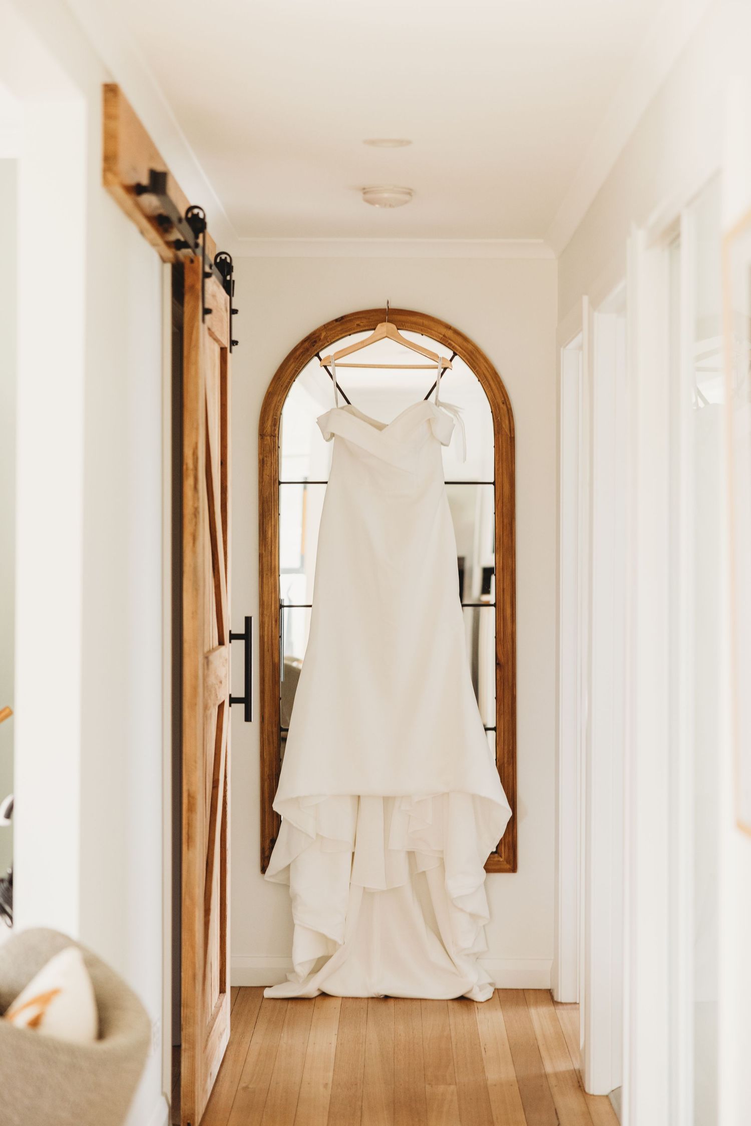 White wedding dress hanging in hallway with arched mirror and sliding barn door.