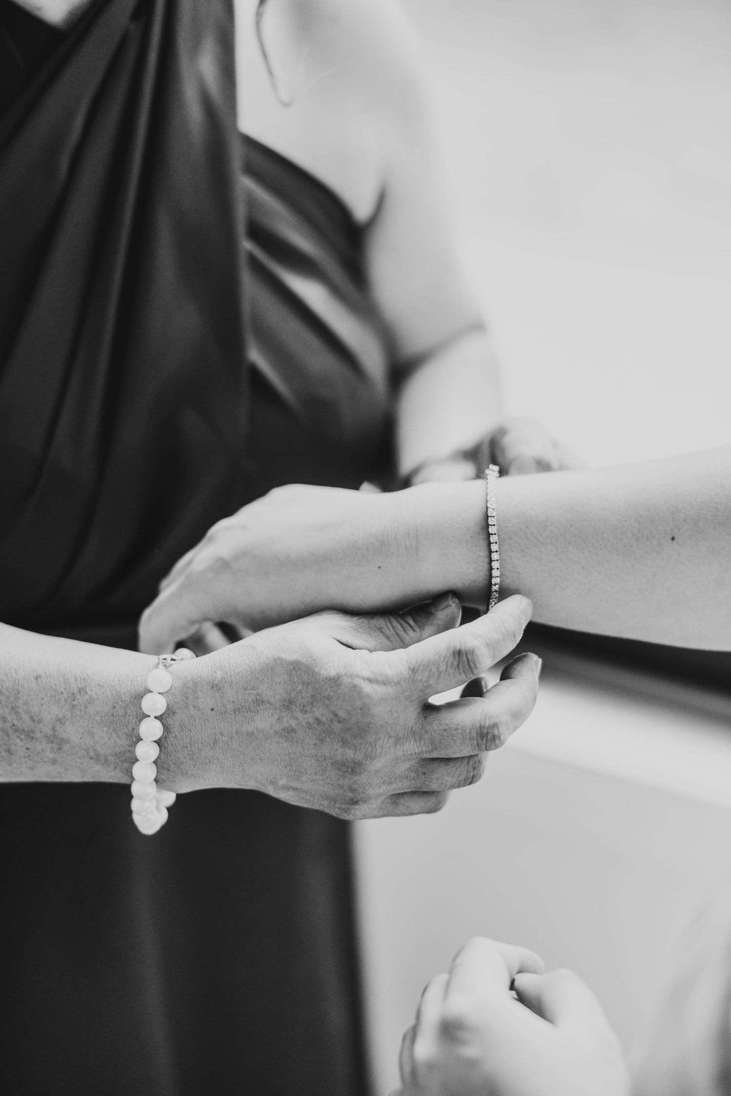 Black and white close-up of hands adjusting jewelry with pearl bracelet.