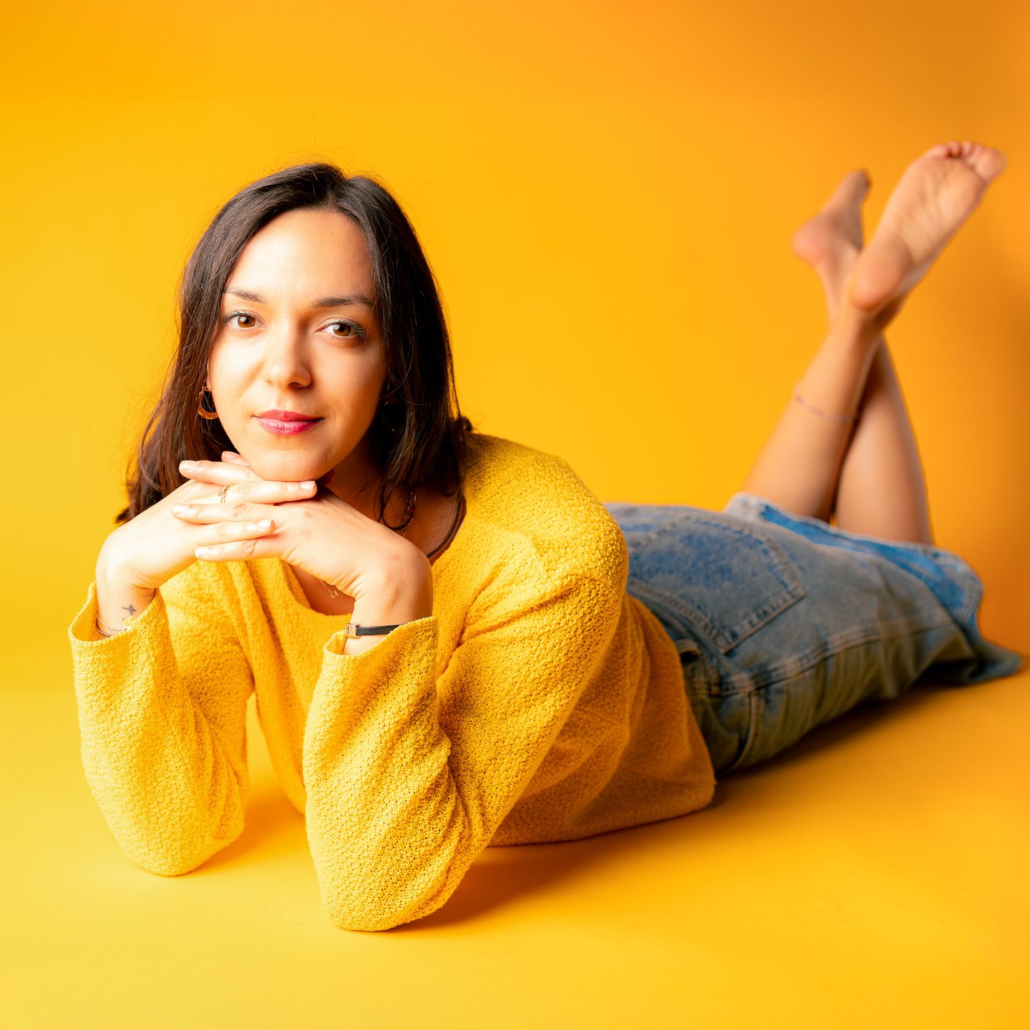 Woman in yellow sweater lying on floor against vibrant yellow background.