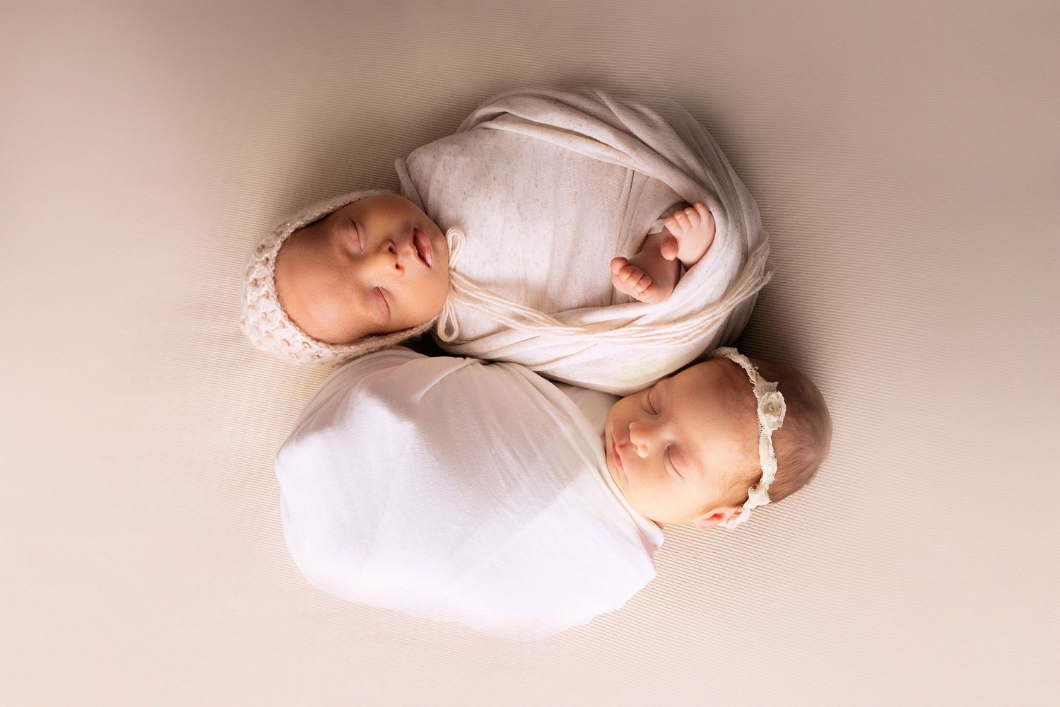 Minimalist newborn photography series with baby wrapped in white against beige backdrop.