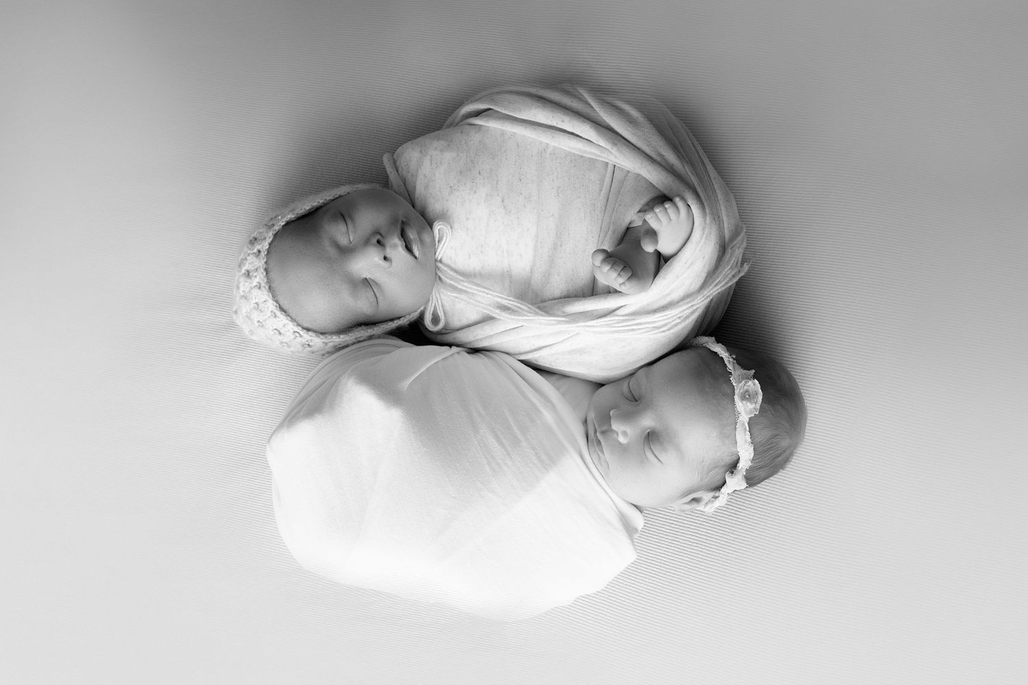 Artistic overhead view of swaddled newborn in white against neutral background.
