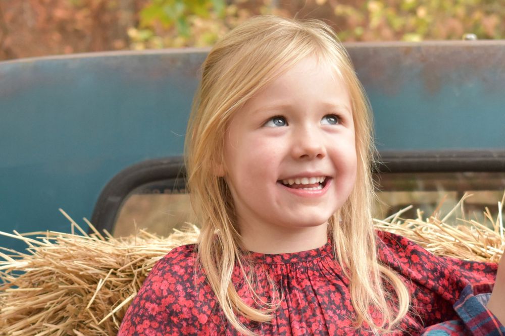 A happy child sits in hay on a vintage truck during an autumn photoshoot.