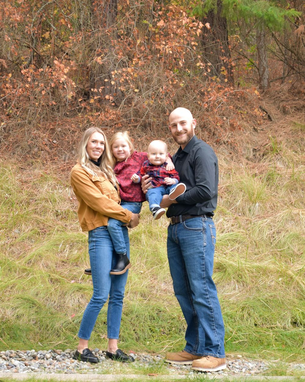 A family poses together on a grassy hillside with fall foliage in the background.