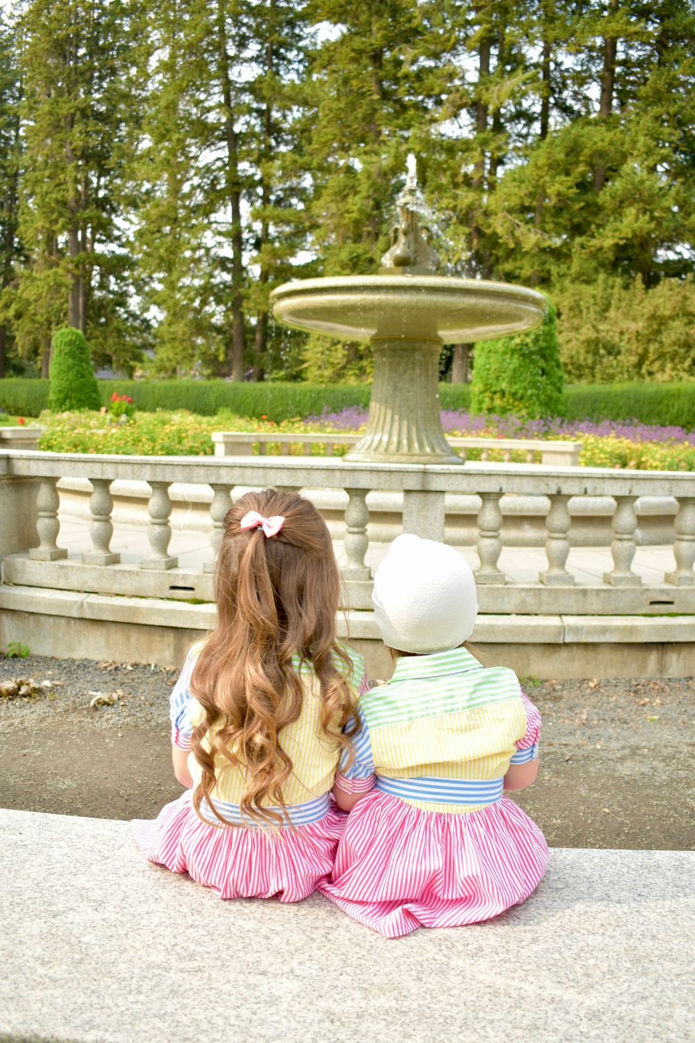 Two matching pink dresses shown from behind on a garden terrace with ornate stone balustrades and green landscaping.