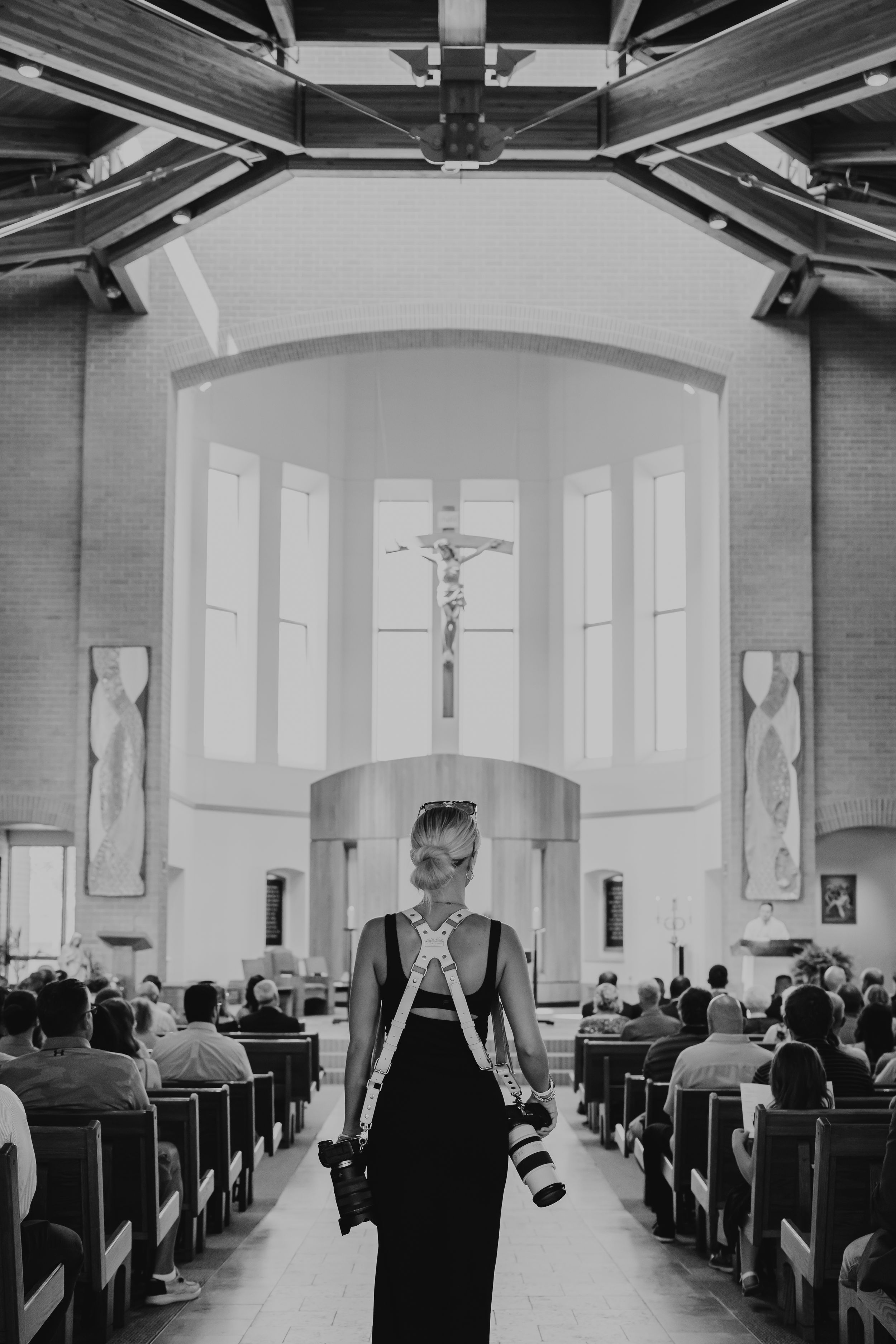 Black and white photo of church interior with rows of pews and arched windows.