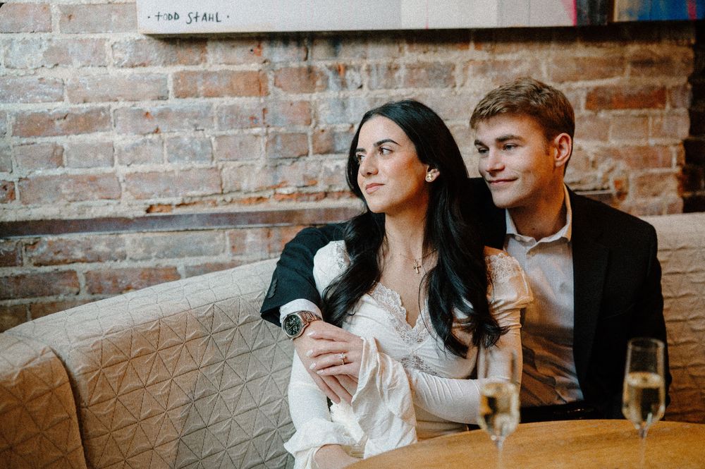 A young couple sits together on a cozy sofa, sharing a romantic moment with champagne glasses nearby.