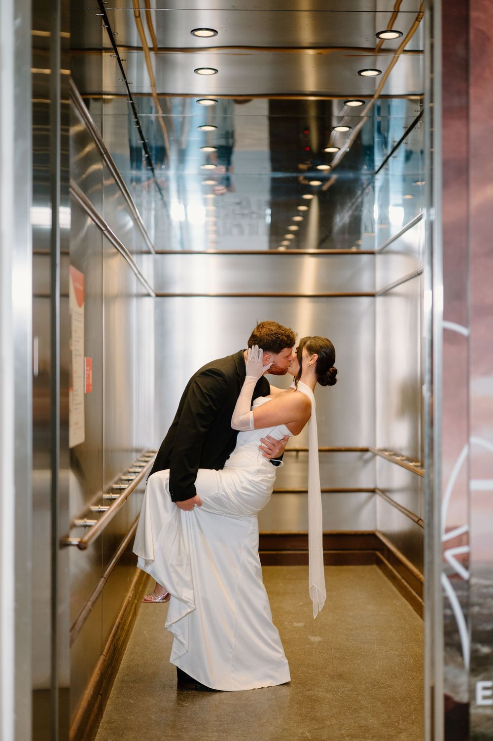 Bride and groom share a romantic dip kiss inside a elegant elevator on their wedding day.
