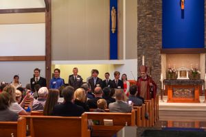 A formal church ceremony with attendees seated in wooden pews and participants standing at the front.