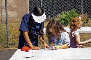Children working on an outdoor art project at a white table.