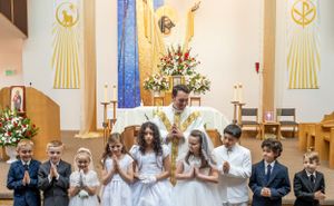 Traditional First Communion celebration in a church with decorative gold religious symbols on the walls.