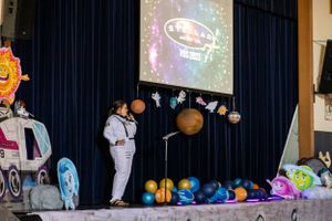 Space-themed stage decoration with planets and navy blue curtains in school auditorium.