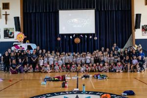 Large group photo of students and staff gathered in a school gymnasium with projection screen.