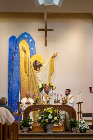 A large Jesus statue with blue and gold backdrop stands behind the altar during a Catholic mass.