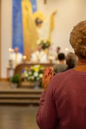 Person praying in a church sanctuary with a blurred altar and decorative banners visible in the background.