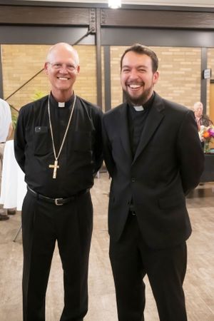 Two clergy members in traditional black clerical attire pose together at a church event.