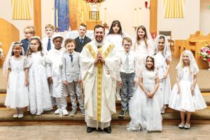 A religious ceremony with children in white dresses and suits standing on church steps.