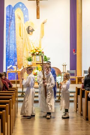 Young altar servers in white robes processing down church aisle with ceremonial items.