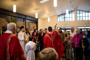 Religious procession with clergy in red vestments and altar servers carrying ceremonial items.