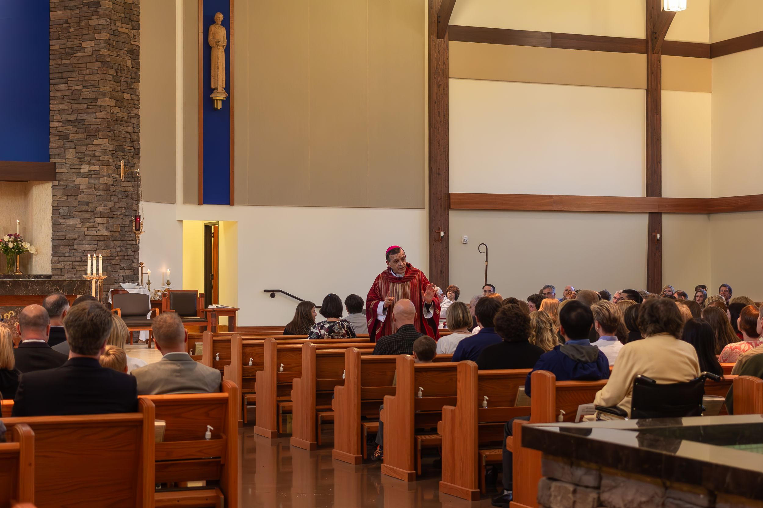 People gathered in church pews while a speaker in red robes addresses the congregation from the front.
