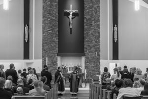 Black and white photograph of a Catholic church service with a crucifix prominently displayed above the altar.