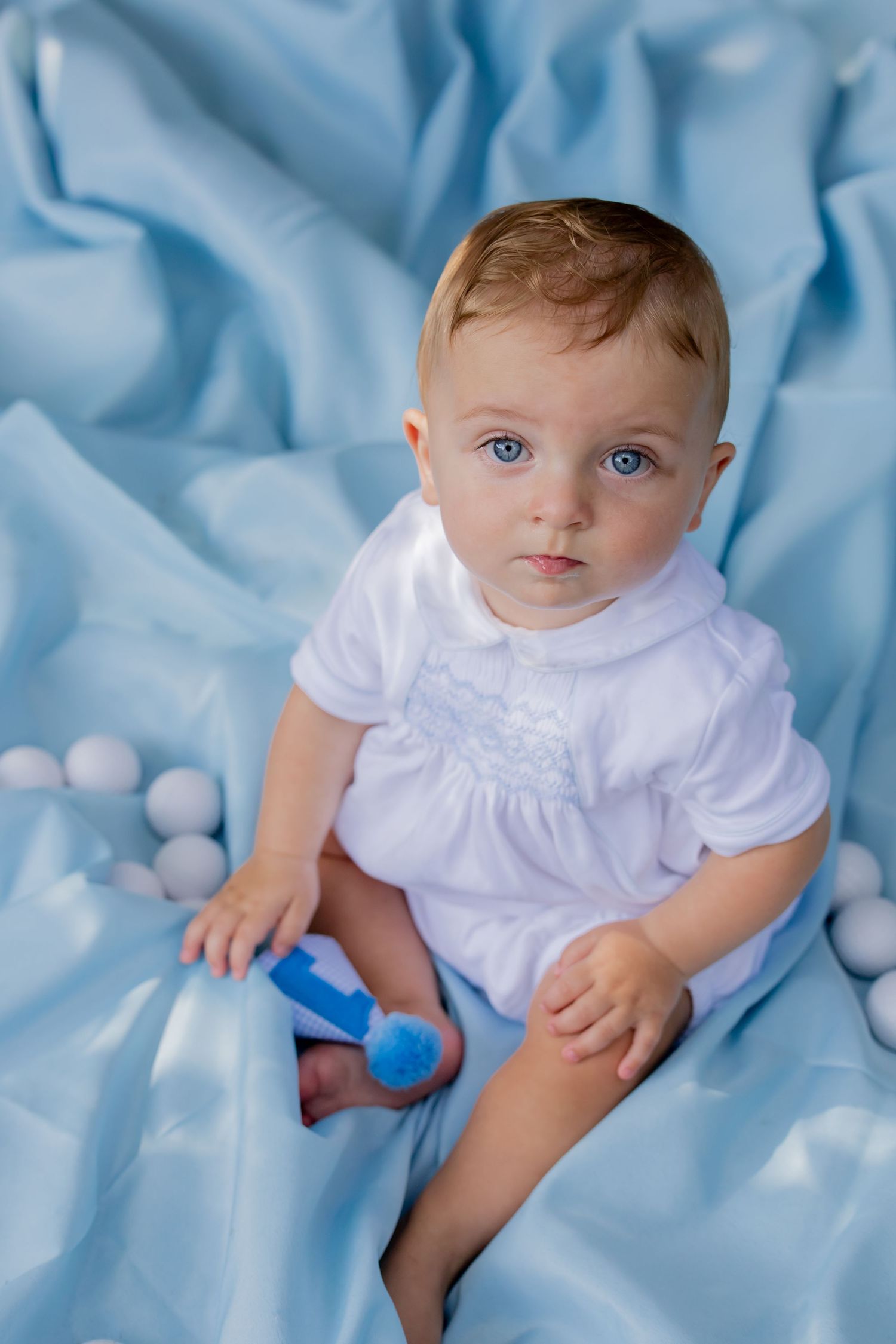 A sleeping newborn baby lies between two plush bunny toys on white bedding.