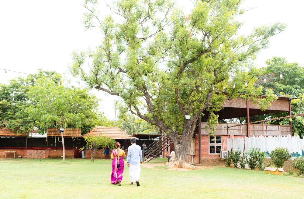 Two people strolling on grass with trees and buildings in the background.